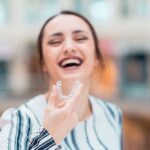 Woman holding an Invisalign tray in front of her and smiling