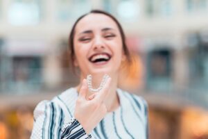 Woman holding an Invisalign tray in front of her and smiling